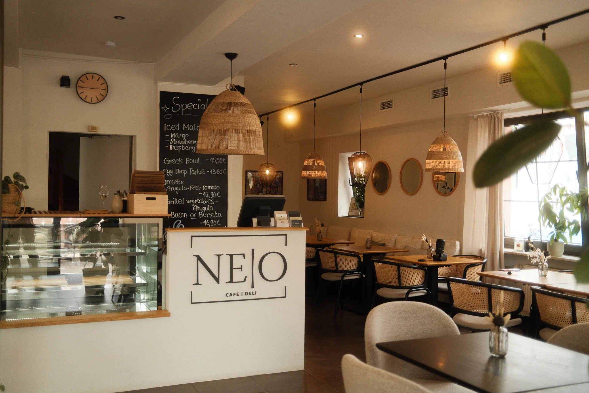 Innenansicht des Neo Café Deli in Ramstein mit gemütlicher Einrichtung, warmem Licht, Holz- und Rattan-Elementen sowie einer modernen Cafétheke mit Tageskarte